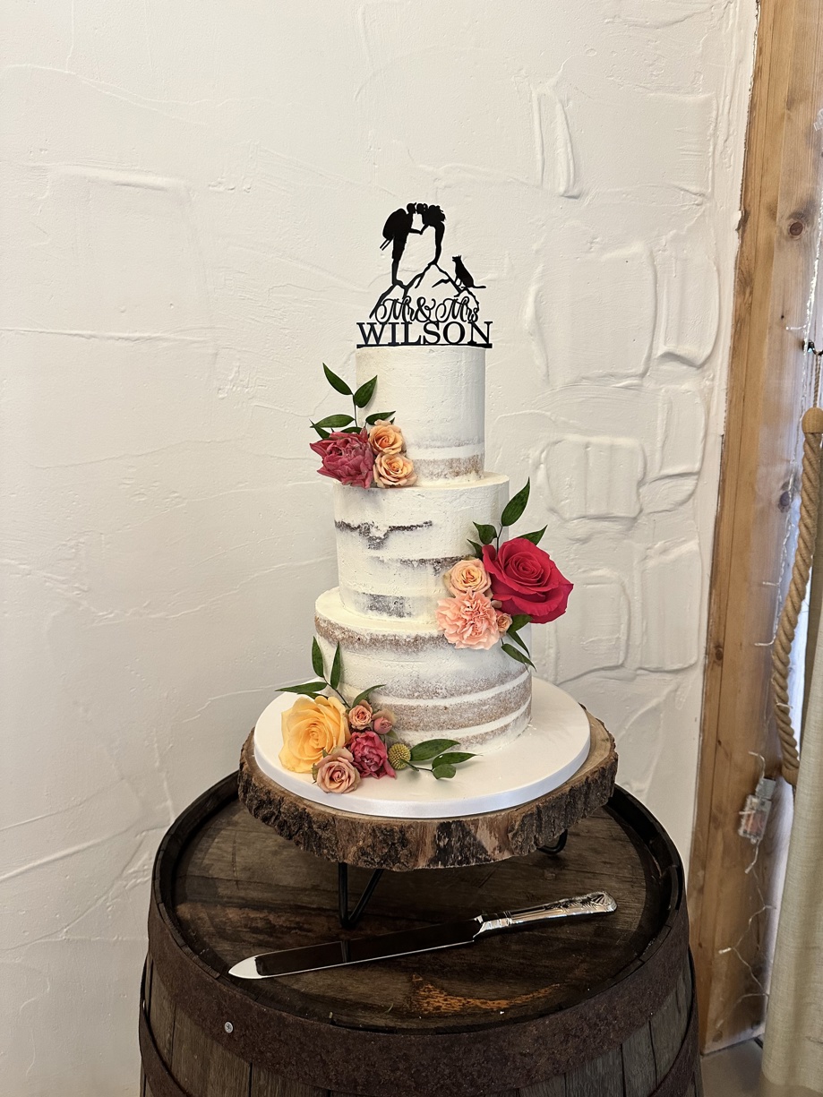 White three-tier cake with red and orange flowers and cake topper with couple kissing
